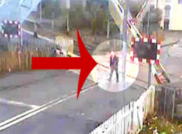 The barriers are coming down and the lights are flashing, but still this man walks across the path of an approaching train